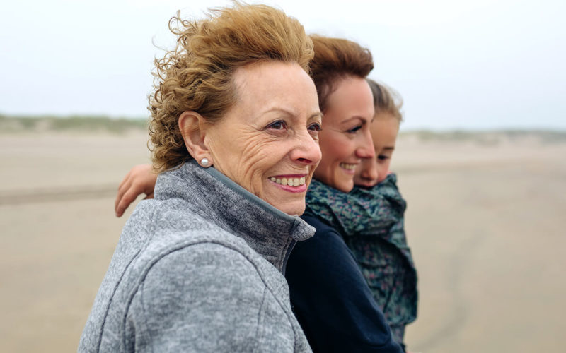 Woman standing on beach with hair blowing in the wind, one is hold a child